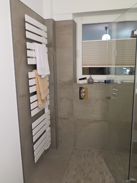 Badezimmer mit großformatigen Wandfliesen, bodengleicher Dusche und Holzoptik-Boden