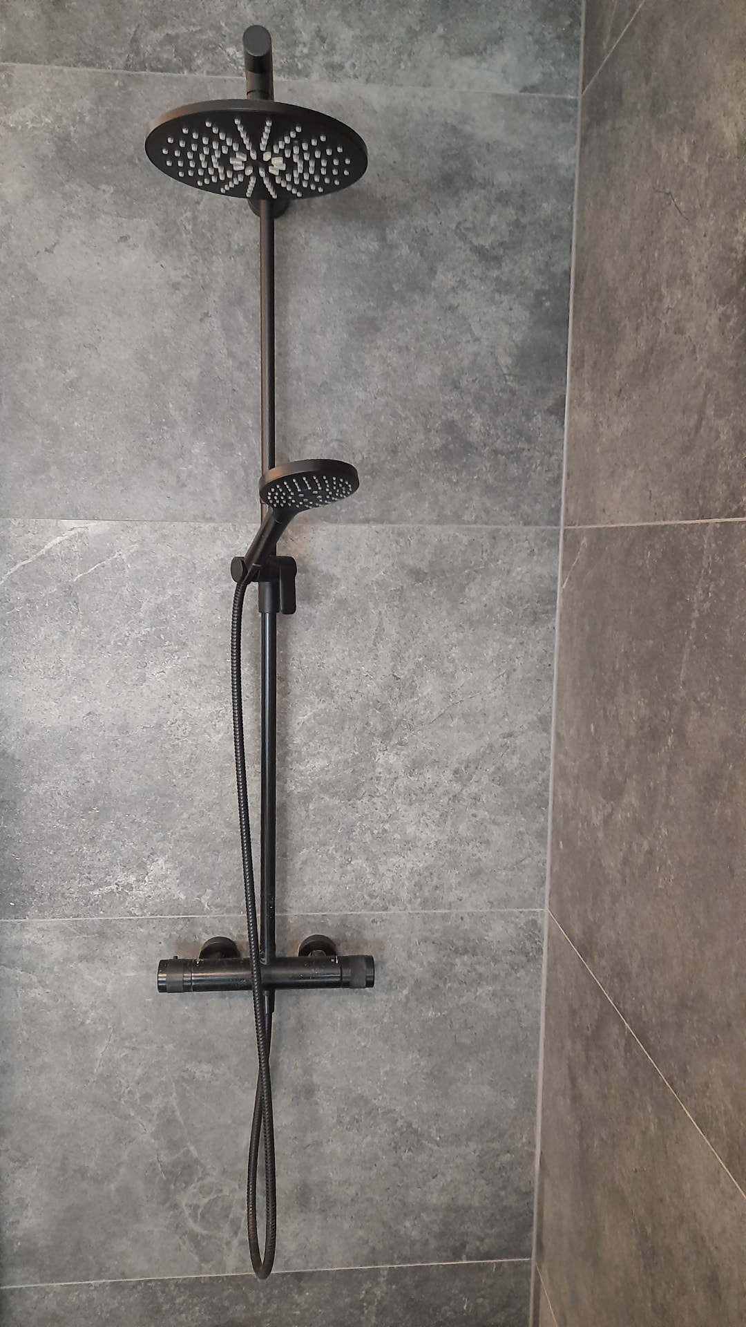 Detail einer Dusche mit schwarzem Regenduschkopf und grauen Großformatfliesen
